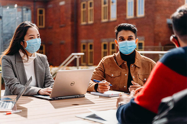 3 students sitting outside at table wearing masks